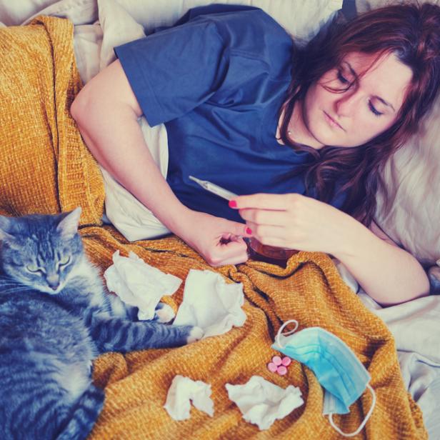 Frau mit Fieberthermometer und Katze im Bett