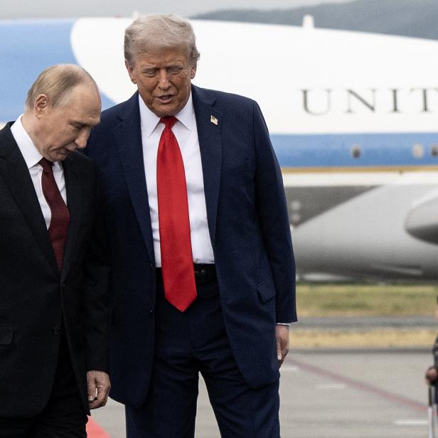 Russlands Präsident Putin und US-Präsident Trump stehen nebeneinander auf einem Flughafen-Rollfeld vor einem Flugzeug, im Hintergrund stehen Soldaten