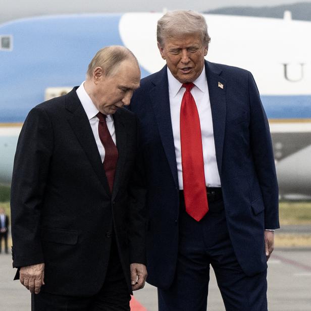 Russlands Präsident Putin und US-Präsident Trump stehen nebeneinander auf einem Flughafen-Rollfeld vor einem Flugzeug, im Hintergrund stehen Soldaten
