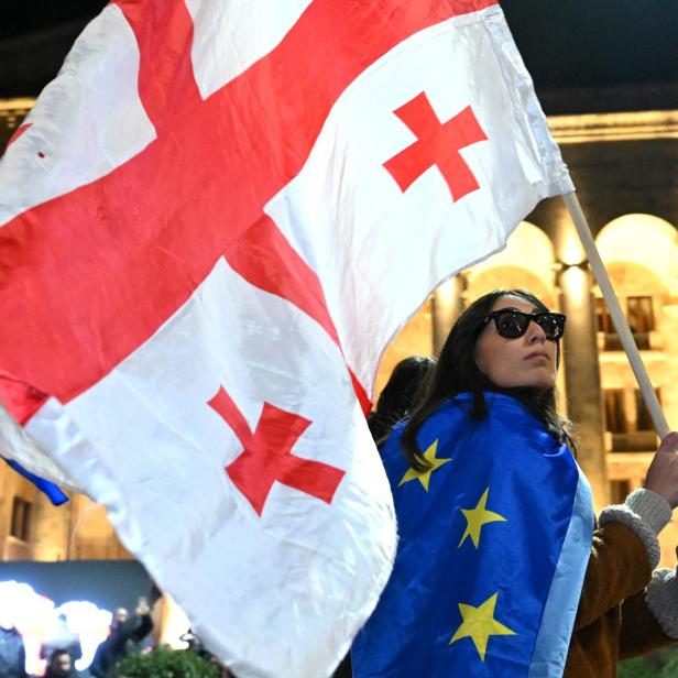 Eine Frau schwenkt eine Georgien-Flagge, sie hat eine EU-Flagge umgehängt.