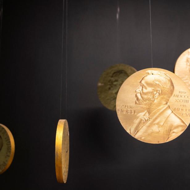 Sechs Nobelpreis-Medaillen hängen an Nylonschnüren vor schwarzem Hintergrund