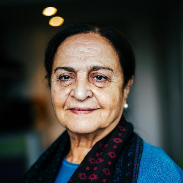 Porträt einer Frau: Sie trägt ein blaues Oberteil und einen schwarzen Schal.