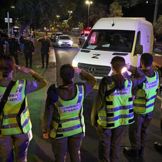 Ein Kleinbus, davor stehen Menschen in Warnwesten und salutieren