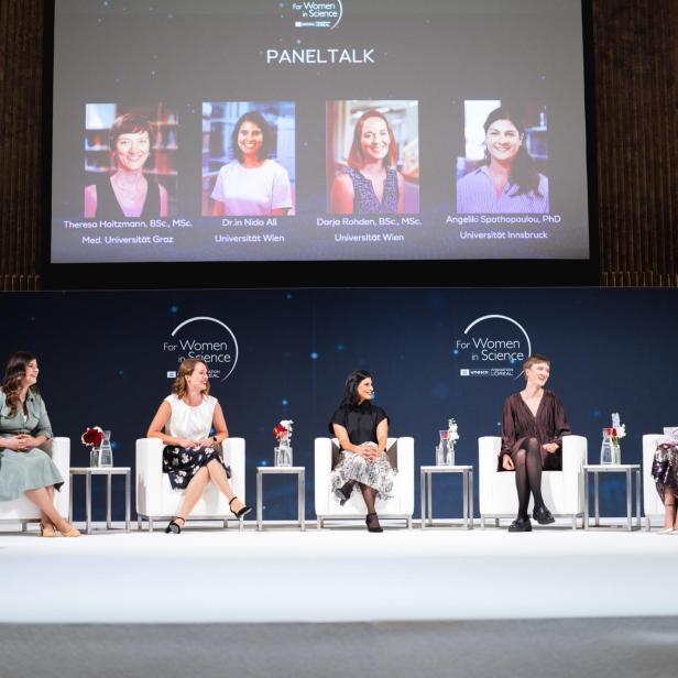 Fünf Frauen sitzen auf einer Bühne bei einer Podiumsdiskussion, im Hintergrund eine Leinwand mit Fotos und Namen der Teilnehmerinnen.