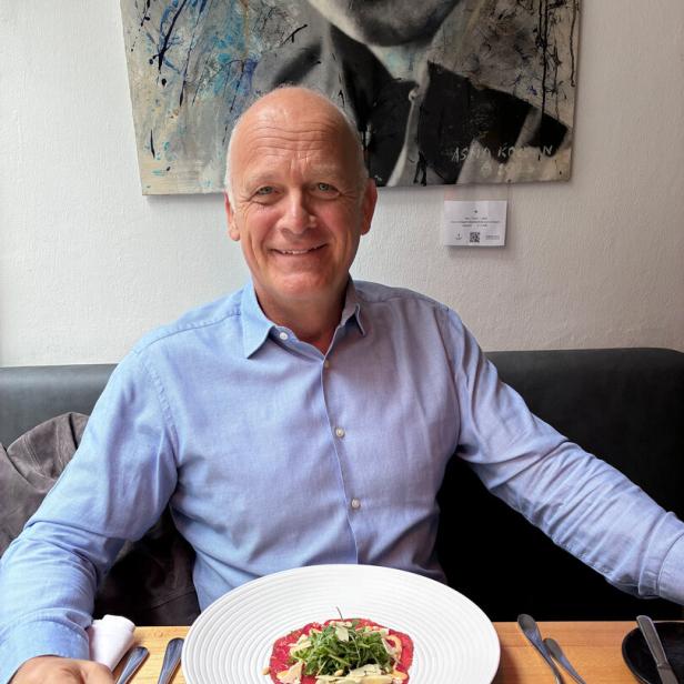 Herwig Straka, Sportmanager Herwig Straka sitzt in blauem Hemd am Restauranttisch, vor sich ein Rindscarpaccio