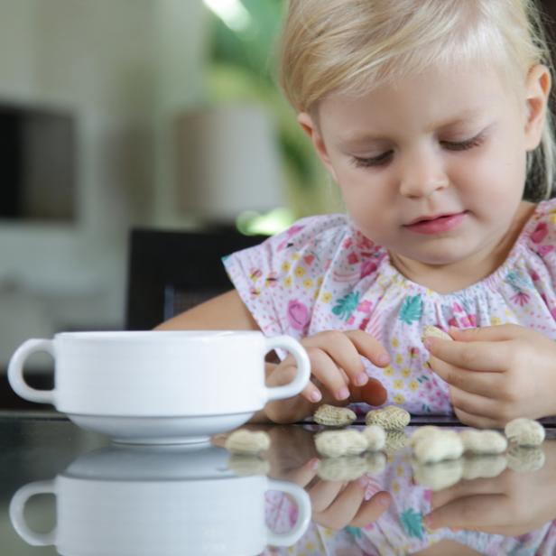 Blondes Mädchen isst Erdnüsse am Küchentisch