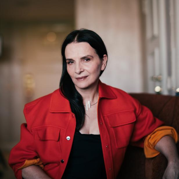Dunkelhaarige Juliette Binoche in roter Jacke blickt uns direkt an