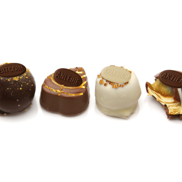 Sechs Pralinen in verschiedenen Formen, jede mit einer goldfarbenen Beschriftung: 'FONDS', 'BITCOIN', 'ANLEIHE', 'KUNST', 'AKTIEN', 'ETF'.