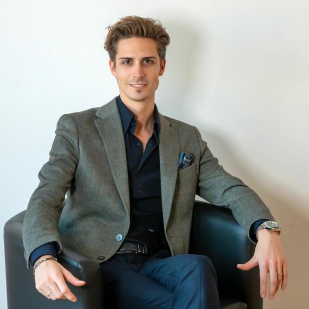 Ein junger Mann sitzt im Anzug auf einem Sessel vor einer weißen Wand. // Expertenberatung beim Immobilienverkauf durch Manuel Hengstler von Hengstler Immobilien GmbH für individuelle Begleitung und fundierte Marktkenntnis in Klagenfurt, Kärnten und Österreich.