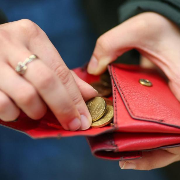 Eine Person öffnet eine rote Geldbörse und nimmt Münzen heraus.