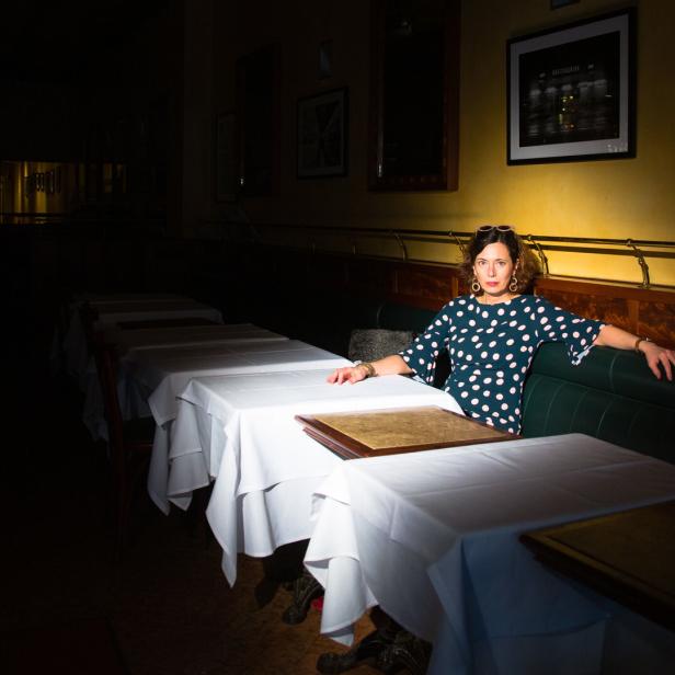 Hell beleuchtete Frau, die an einem Restauranttisch in einem ansonsten ganz abgedunkelten Raum sitzt