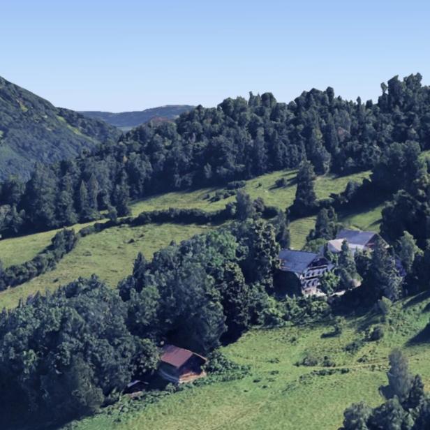 Eine grüne Berglandschaft. Zwischen den Bäumen stehen alte Häuser.