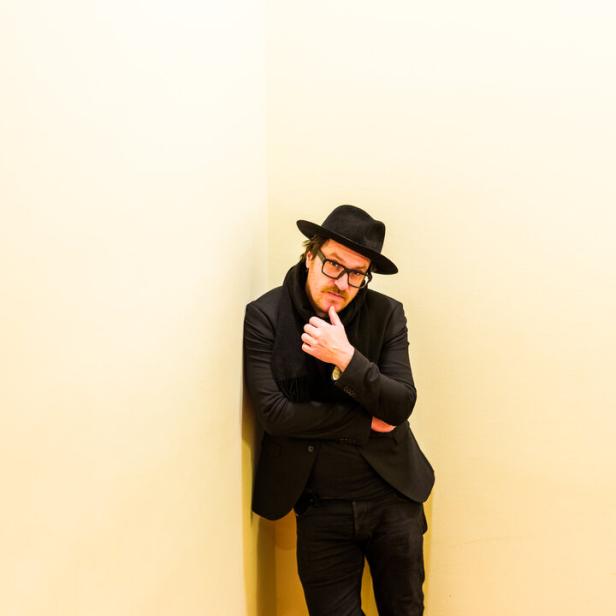 Parov Stelar alias Marcus Füreder steht im Mantel und mit Hut am Ende einer Treppe.