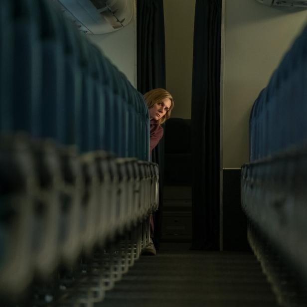 Frau, die in der letzten Reihe einer Flugzeugkabine sitzt, blickt den Gang zwischen den sonst menschenleeren Sitzreihen entlang