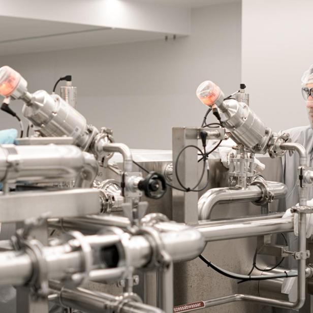 Zwei Personen in Schutzkleidung und Haarnetzen bedienen komplexe Edelstahlrohrleitungen in einem Maschinenraum.