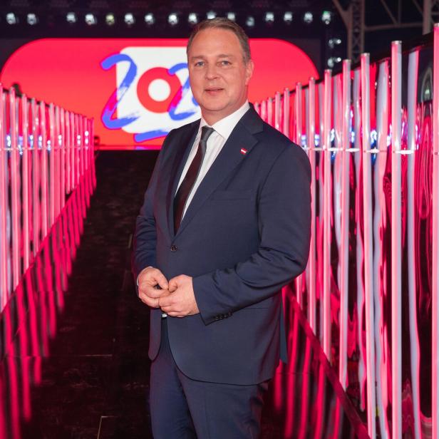 Mann in dunkelblauem Anzug posiert in einem rosaroten, neonbeleuchteten Korridor.