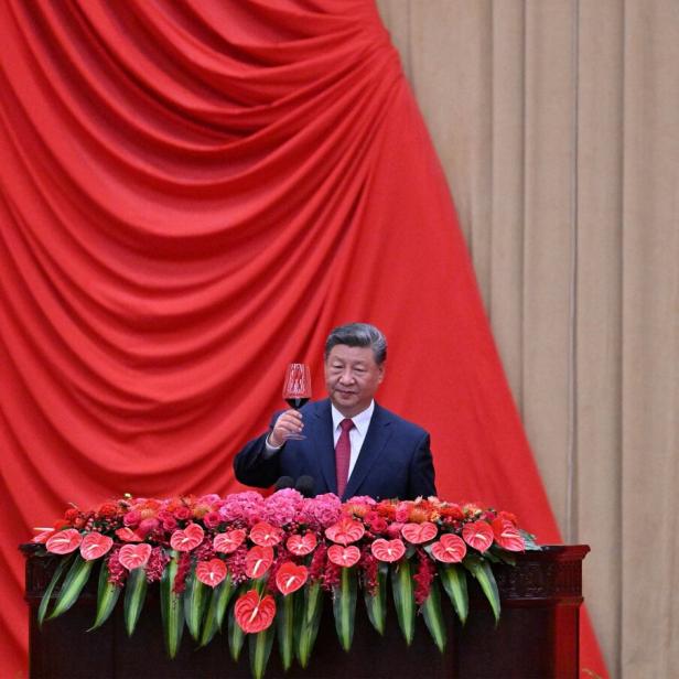 Chinas Präsident Xi Jinping prostet mit einem Glas Rotwein von einem blumengeschmückten Pult