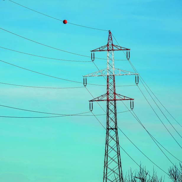 Strommast mit rot-weiß lackiertem Stahlgitter und mehreren Hochspannungsleitungen vor blauem Himmel.
