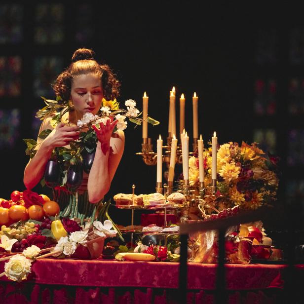 Junge Frau bedient sich an einem üppig beladenen Buffettafel in schwarzem Raum