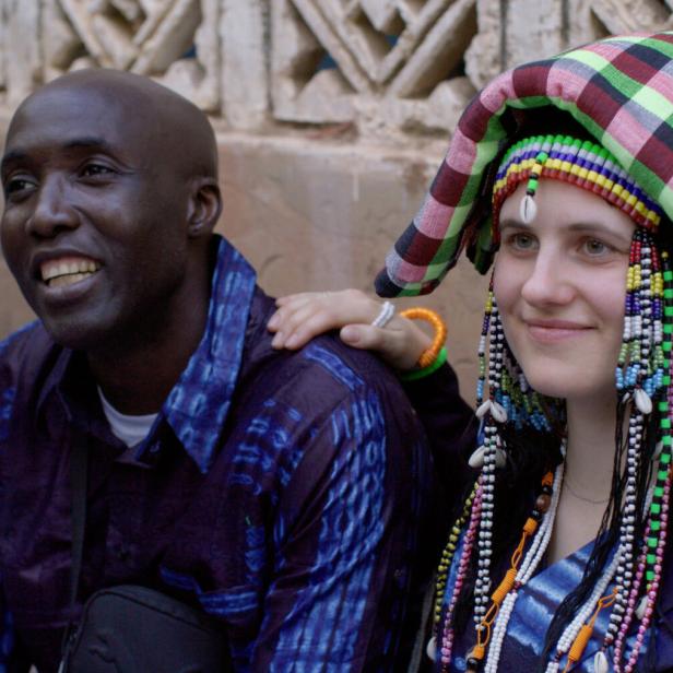 Victoria Preuer und Siaka Touray sind ein Paar. Sie, mit traditionellem Kopfschmuck, legt ihre Hand auf die Schulter des lächelnden Mannes.