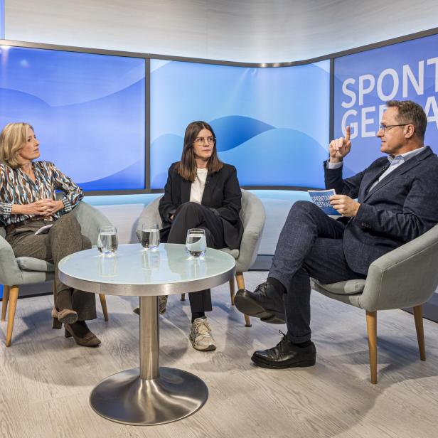 Drei Personen sitzen in Sesseln um einen runden Glastisch mit drei Wassergläsern, im Hintergrund Schriftzug 'SPONTAN GEFRAGT'.