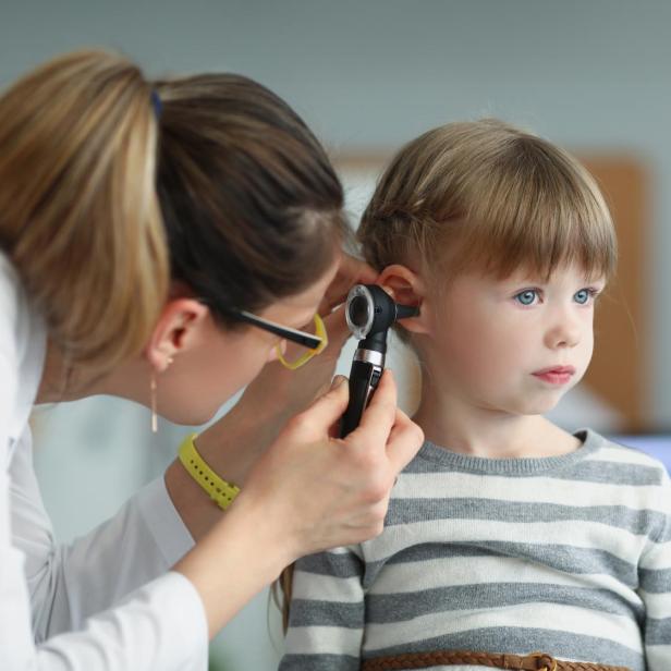 Kinderarzt mit Blick auf das Ohr eines kleinen Mädchens mit Otoskop.