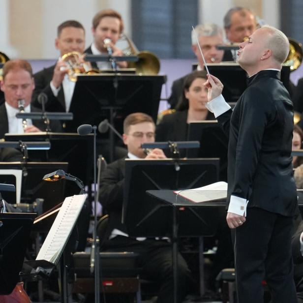 Dirigent mit erhobenem Taktstock leitet ein Orchester.  