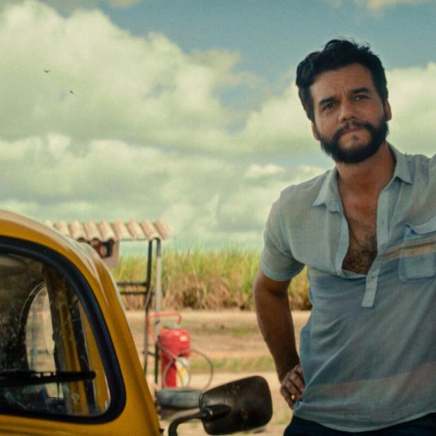 Der Schauspieler Wagner Moura lehnt an einer Säule, neben ihm ein gelbes Auto