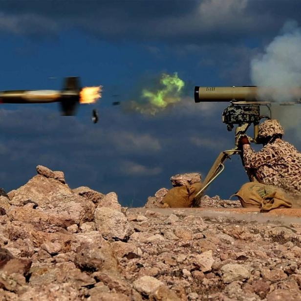 Ein Geschütz schießt eine Rakete ab, ein Soldat hockt unter dem Geschütz.