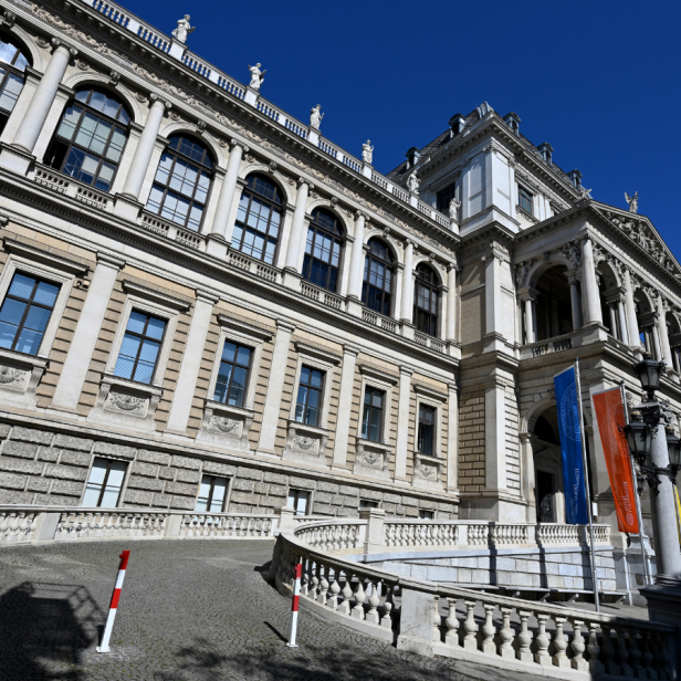 Hauptgebäude der Universität Wien mit bunten Fahnen bei klarem Himmel.