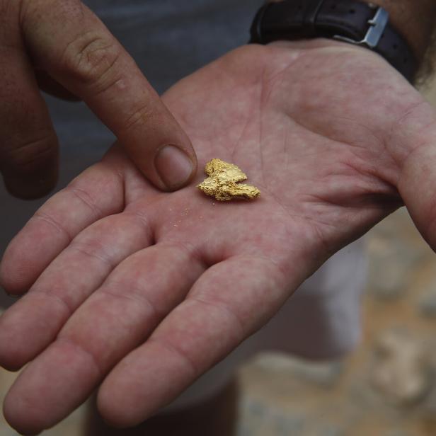 Ein Mann hält ein großes Stück Gold in seiner Hand, er zeigt mit einem Finger darauf.