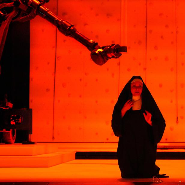 Szenenbild aus "Sancta": eine Nonne kniet in rotem LIcht auf der Bühne, hinter ihr ein Kamera-Kran