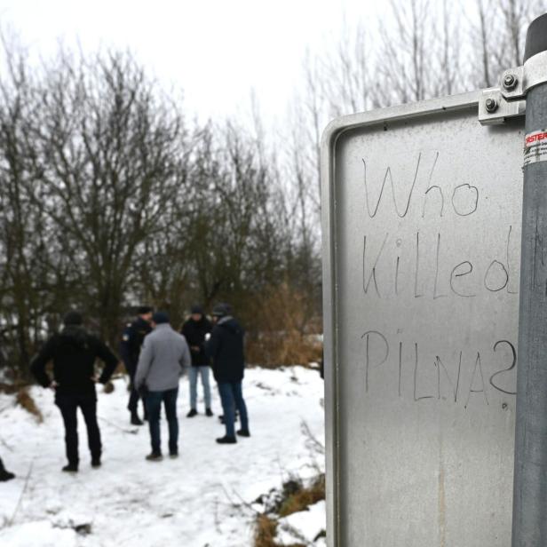 Who killed Pilna? steht auf einem Schild, dahinter stehen Leute
