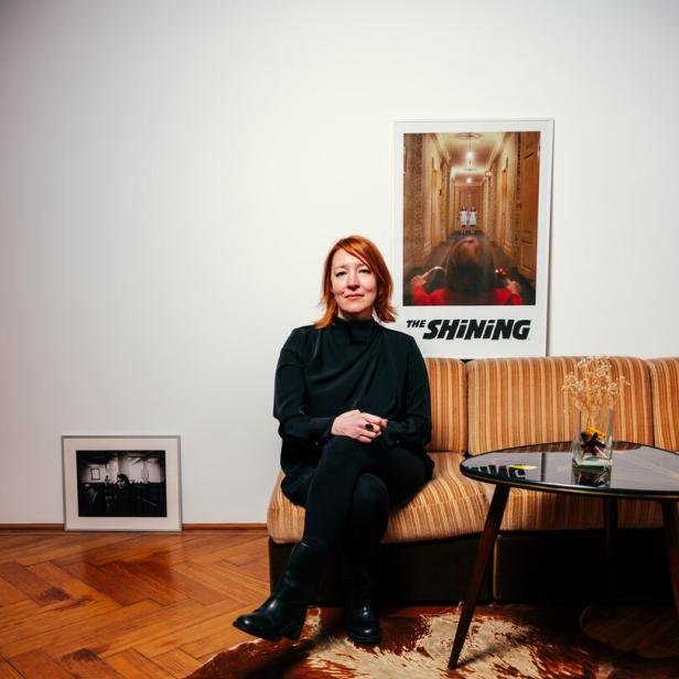 Barbara Kaufmann sitzt auf einem Sofa, hinter ihr ein Filmposter von The Shining