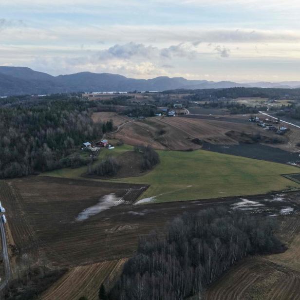 Eine Luftaufnahme des norwegischen Dorfs Ulefoss. Man sieht grüne Felder und Wälder, links im Bild kann man den See und entfernte Hügel entdecken.