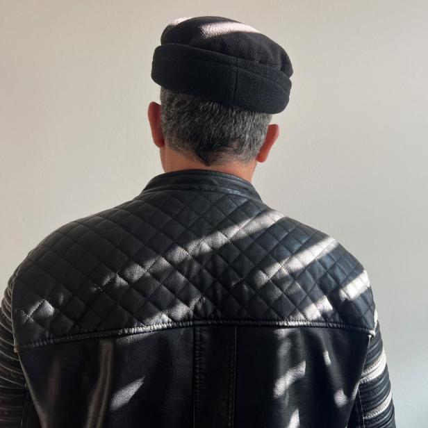 Syrischer Familienvater mit aufgestellter Mütze und schwarzer Lederjacke von hinten 