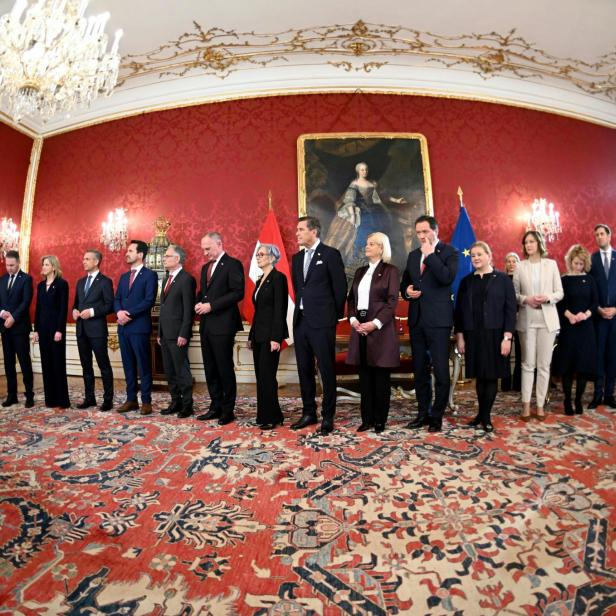 Mitglieder der österreichischen Bundesregierung stehen in einem prunkvollen Saal während einer offiziellen Zeremonie nebeneinander.