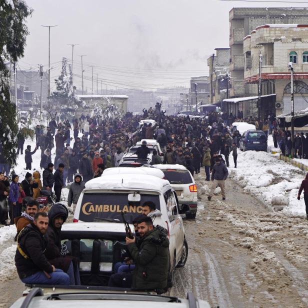 Ein Konvoi an Pickups mit Kämpfern darauf fährt durch eine schneebedeckte Stadt (Kobane).