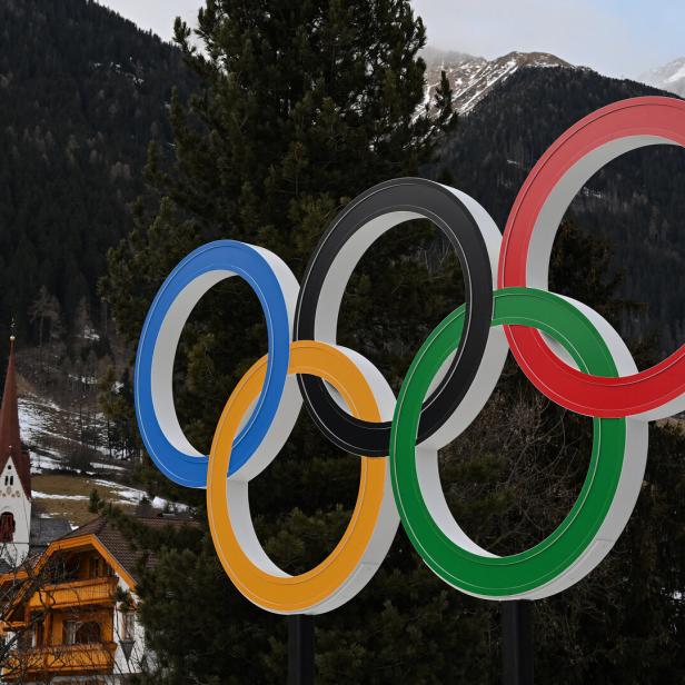 Eine plastische Darstellung der Olympischen Ringe, installiert vor einem Dorfpanorama in Italien