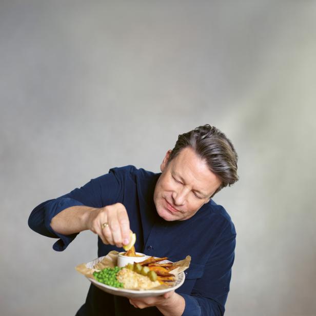 Jamie Oliver blickt auf einen Teller mit Erbsen und paniertem Fisch.