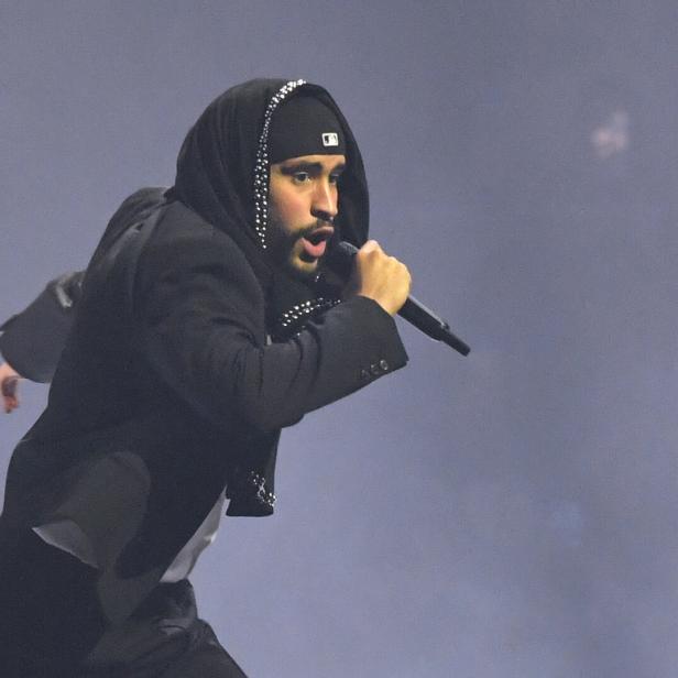 Der Musiker Bad Bunny singt in schwarzem Outfit bei einem Auftritt in sein Mikrofon.