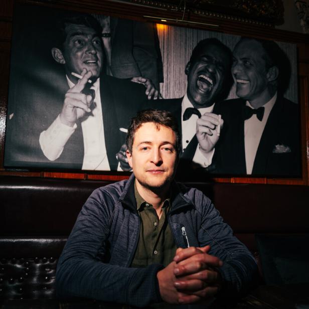 Der Satiriker Fritz Jergitsch vor einem Foto, das Dean Martin, Sammy Davis Jr. und Frank Sinatra zeigt
