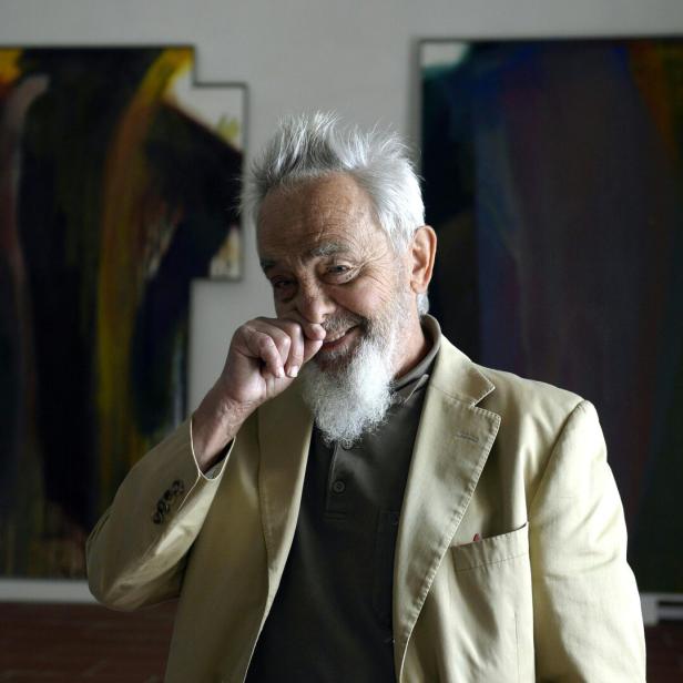 Der Maler Arnulf Rainer, schelmisch lachend, vor zwei seiner Gemälde 