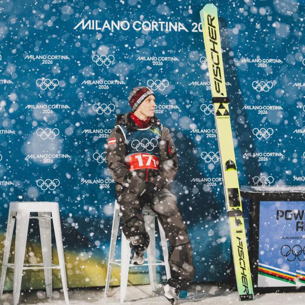 Der Skispringer Jan Hörl sitzt vor einer Werbewand auf einem Barhocker in heftigem Schneetreiben