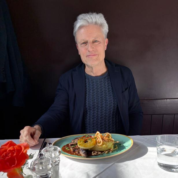 Florian Scheuba sitzt an einem gedeckten Tisch