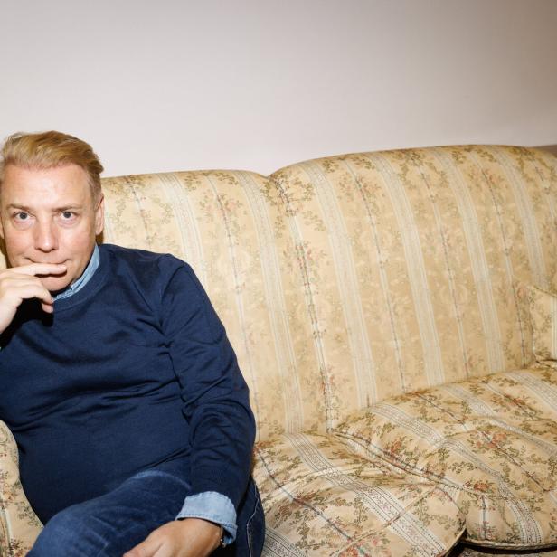 Modedesigner Atil Kutoglu sitzt auf einem gelb-braunen Sofa