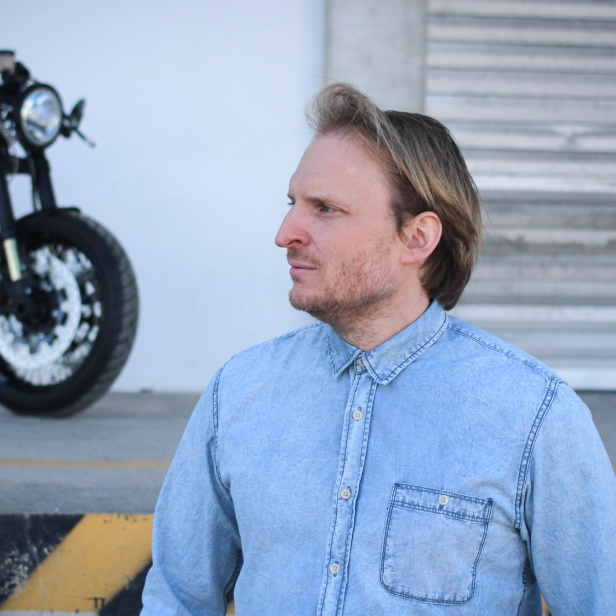 Ein Mann steht in einer Jeansjacke vor einem Motorrad