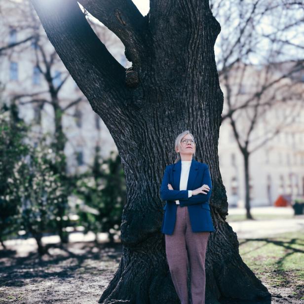 Grünen-Chefin Leonore Gewessler lehnt sich an einen Baum vor dem Parlament