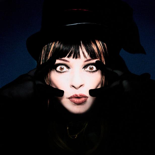 Das grell beleuchtete Gesicht der Musikerin Nina Hagen, die aus der Dunkelheit mit aufgerissenen Augen in die Kamera blickt