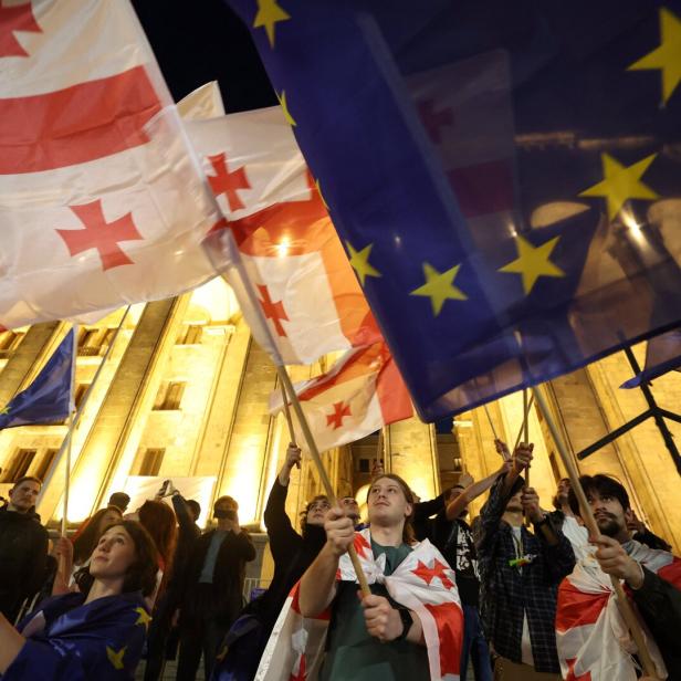 Protestierende schwenken EU- und Georgien-Flaggen vor dem georgischen Parlament im Hintergrund.